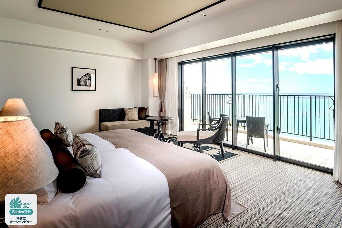 Een hotelkamer met een groot bed, een bureau en een balkon met uitzicht op zee.
