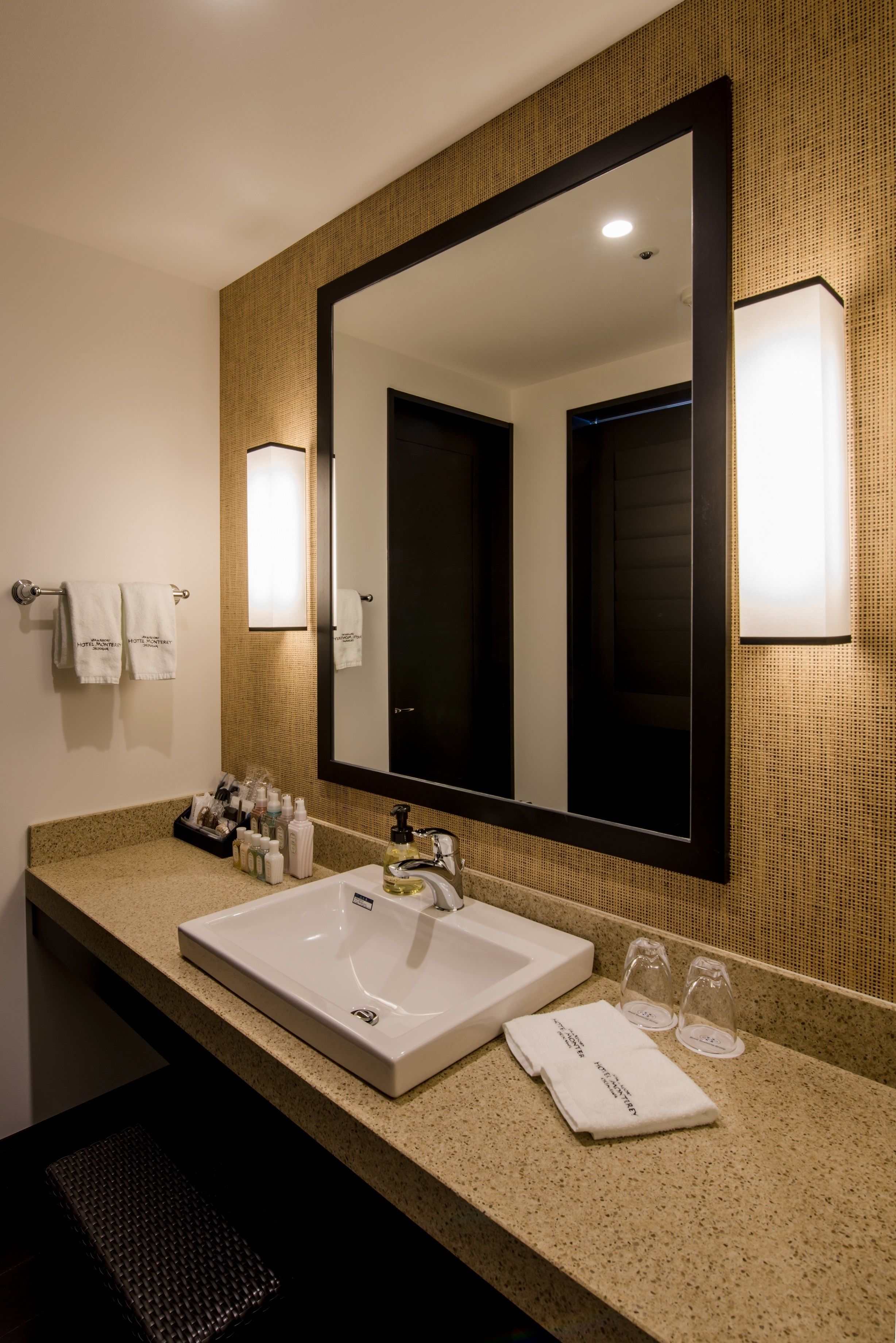 Un baño de hotel con un espejo grande, un lavabo blanco y una encimera con artículos de aseo.