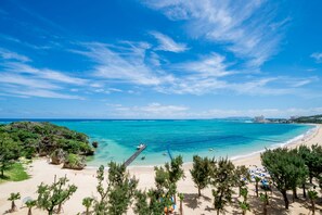 Een strand met helder turquoise water, een steiger en een hotel op de achtergrond.