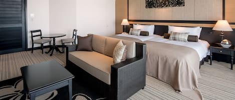 A hotel room with a bed, two bedside tables, a sofa, a small table, and a ceiling fan.