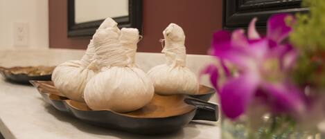 A kitchen counter with a pan holding two wrapped items, possibly food, and a vase with purple flowers.