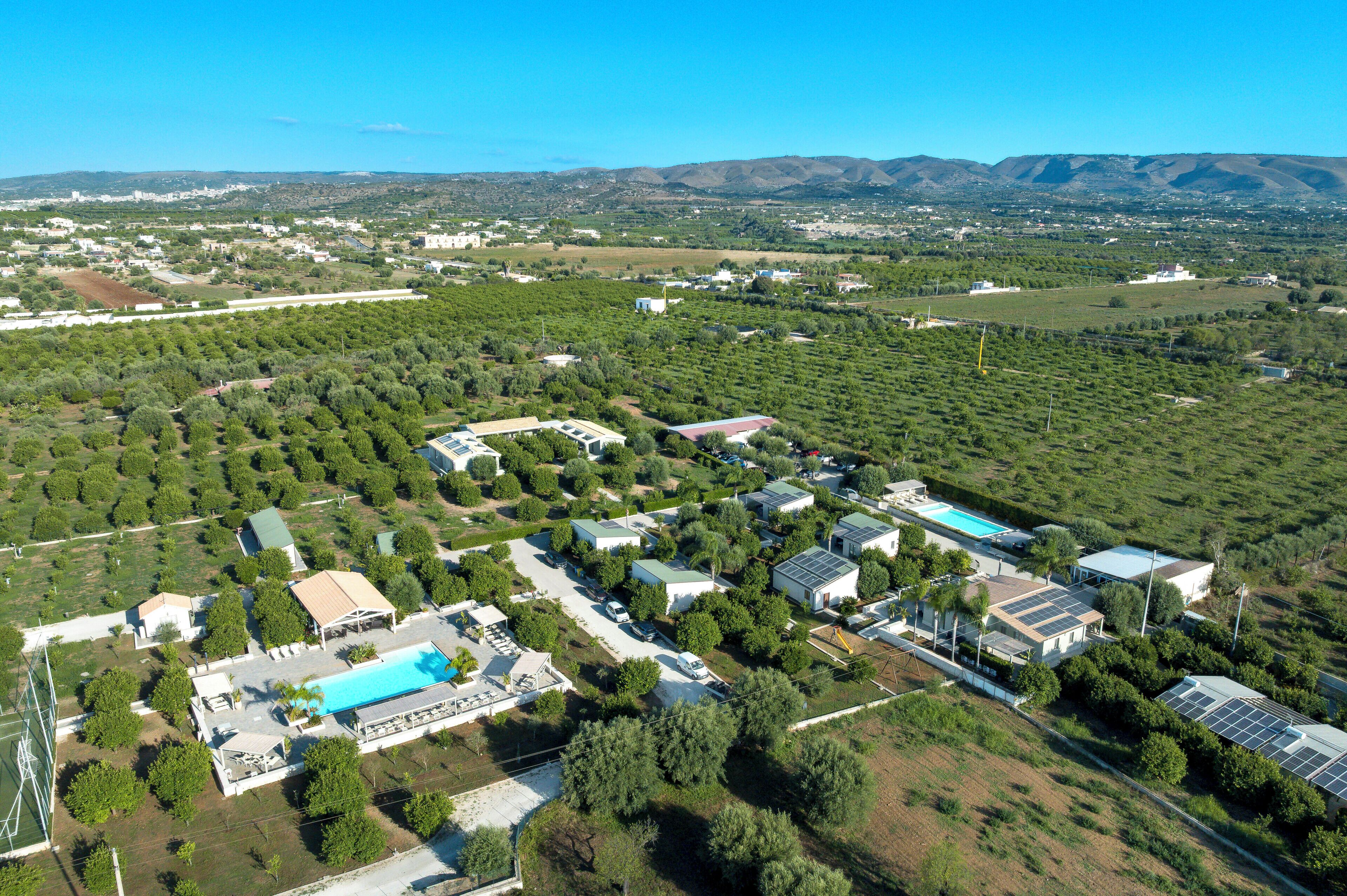 An aerial view of a resort with multiple buildings, a swimming pool, and solar panels.
