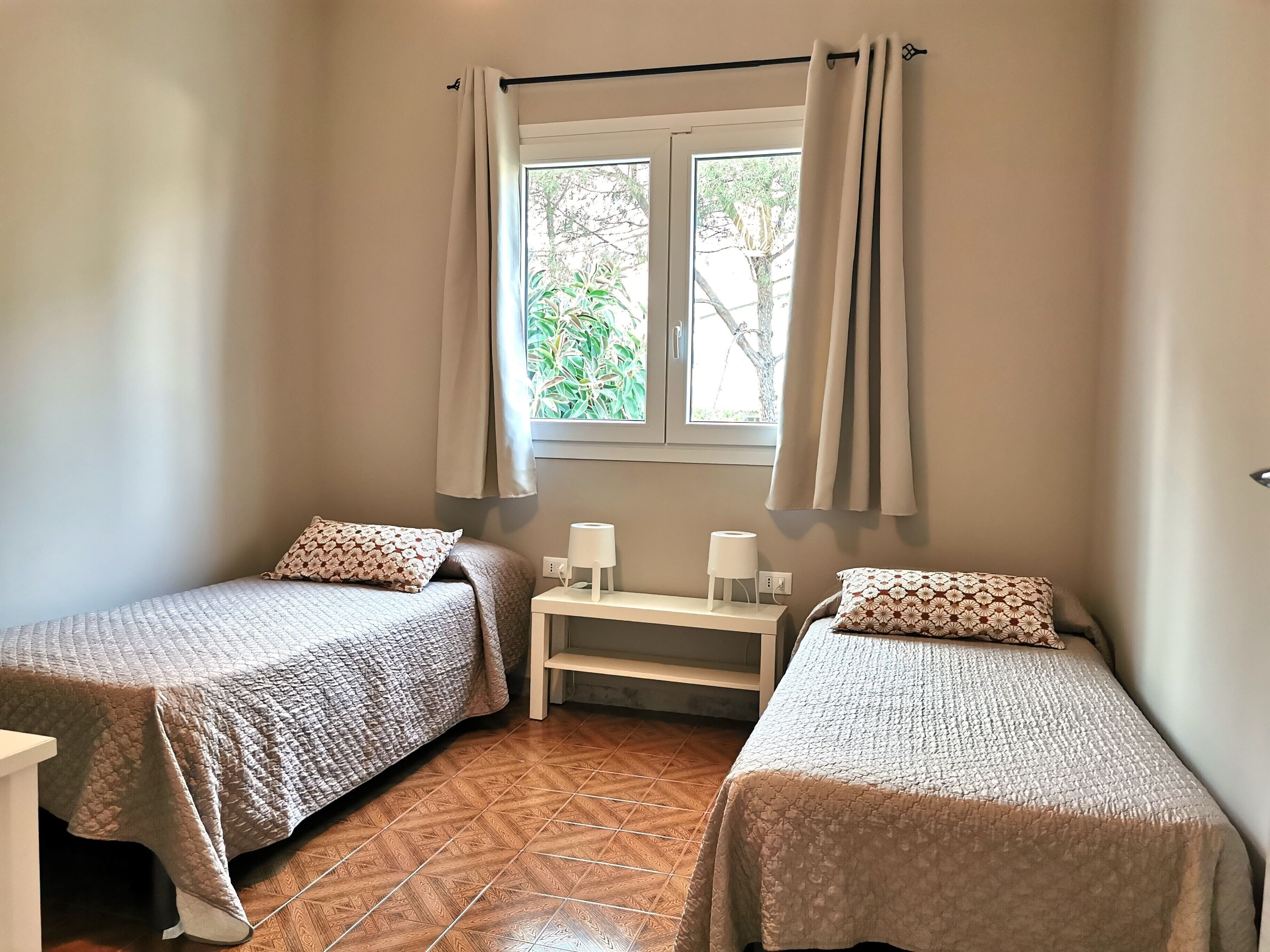 A bedroom with two single beds, a nightstand with a lamp, and a window with curtains.