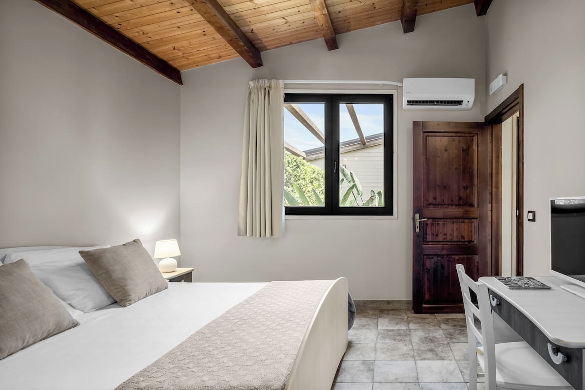 Un dormitorio con cama, mesita de noche, lámpara, ventana y un escritorio con silla.