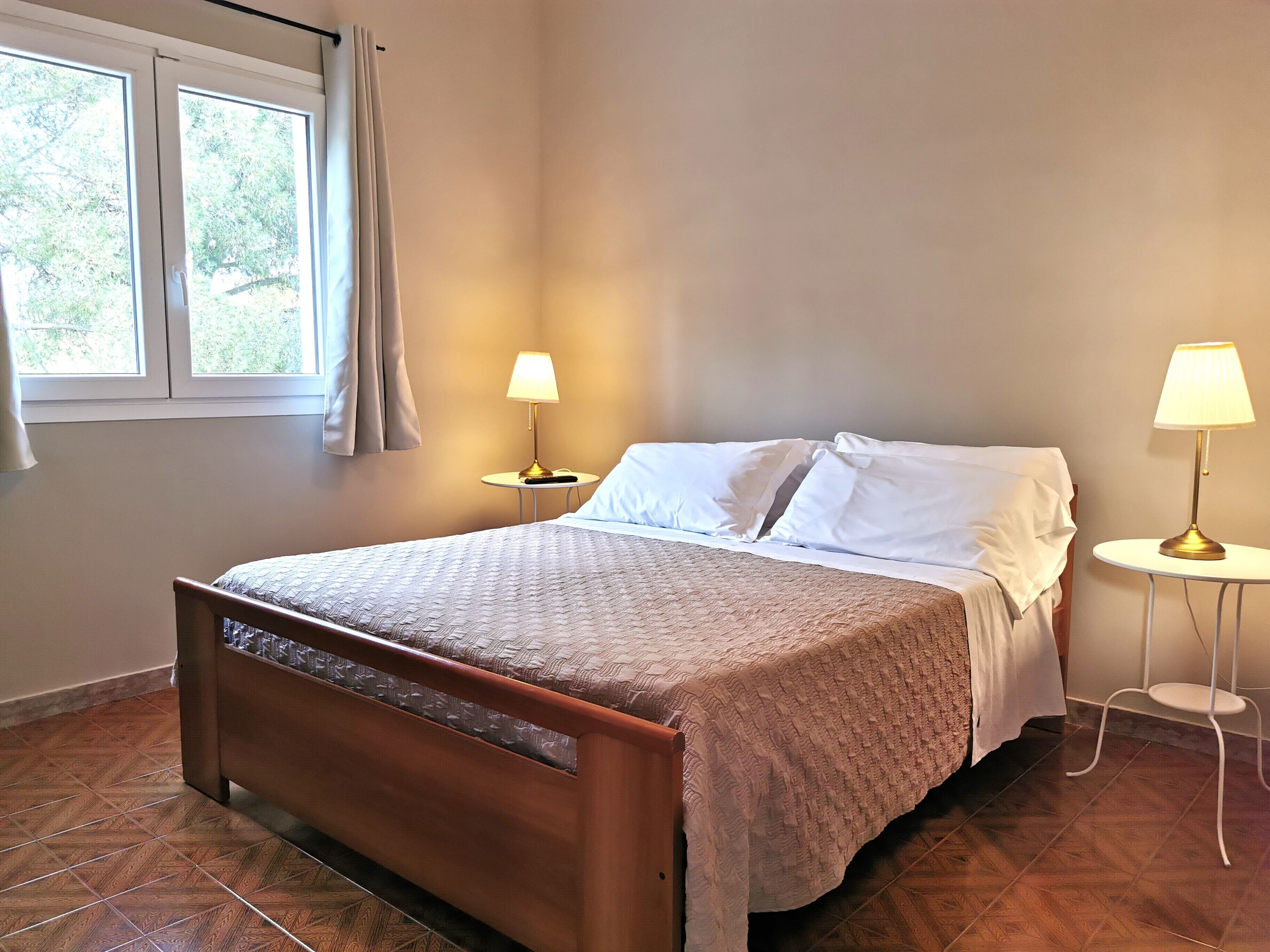 A neatly made bed with a wooden headboard, two bedside lamps, and a window with curtains.