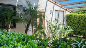 Een huis met een overdekte veranda, palmbomen en een verzorgde tuin.