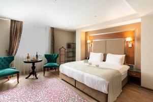 A hotel room with a large bed, two chairs, a small table, and a bedside table with a lamp.