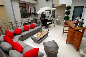 Un espacio exterior moderno con un sofá seccional gris, cojines rojos, un sillón mecededor y una mesa de madera con botellas.