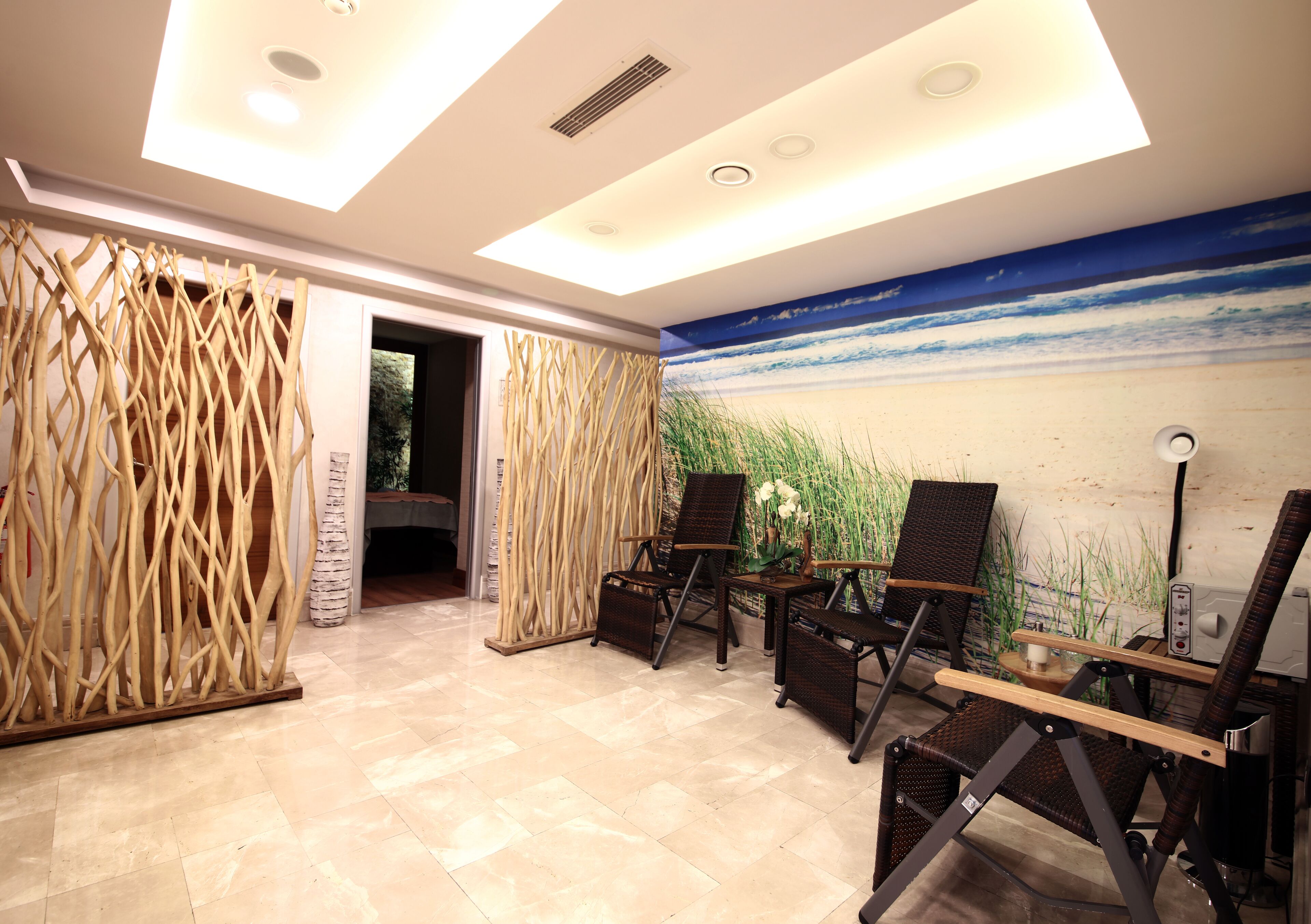 A modern room with a beach mural, a wooden decorative screen, and three wicker chairs with a small table.