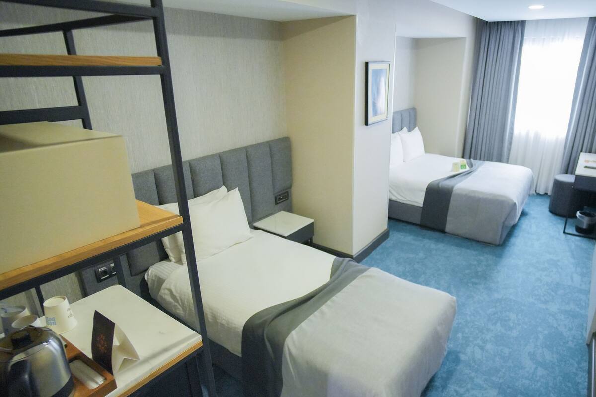 A hotel room with two beds, a desk, a chair, a TV, and a window with curtains.