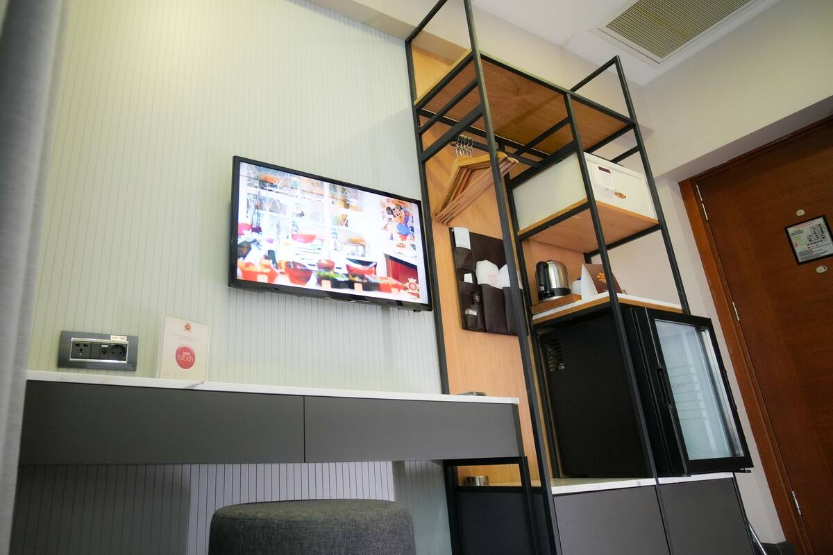 A modern room with a TV mounted on the wall, a small desk with a chair, and a loft-style bed with a wooden ladder.