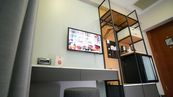 A modern room with a TV mounted on the wall, a small desk with a chair, and a loft-style bed with a wooden ladder.
