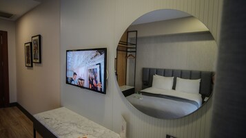 Habitación de hotel con una cama, un televisor montado en la pared y un espejo circular que refleja parte del cuarto.