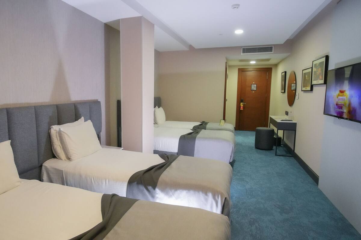 A hotel room with two single beds, a desk, a chair, a television, and a door leading to another room.