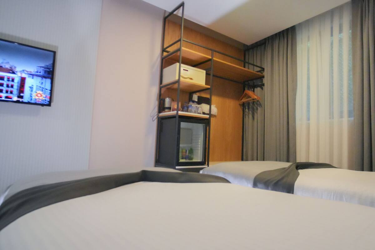 A hotel room with two beds, a built-in wardrobe, a television on the wall, and a window with curtains.