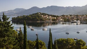 A coastal town with boats docked along the shore, surrounded by mountains and dense greenery. - Hotel Supetar Cavtat (Konavle)