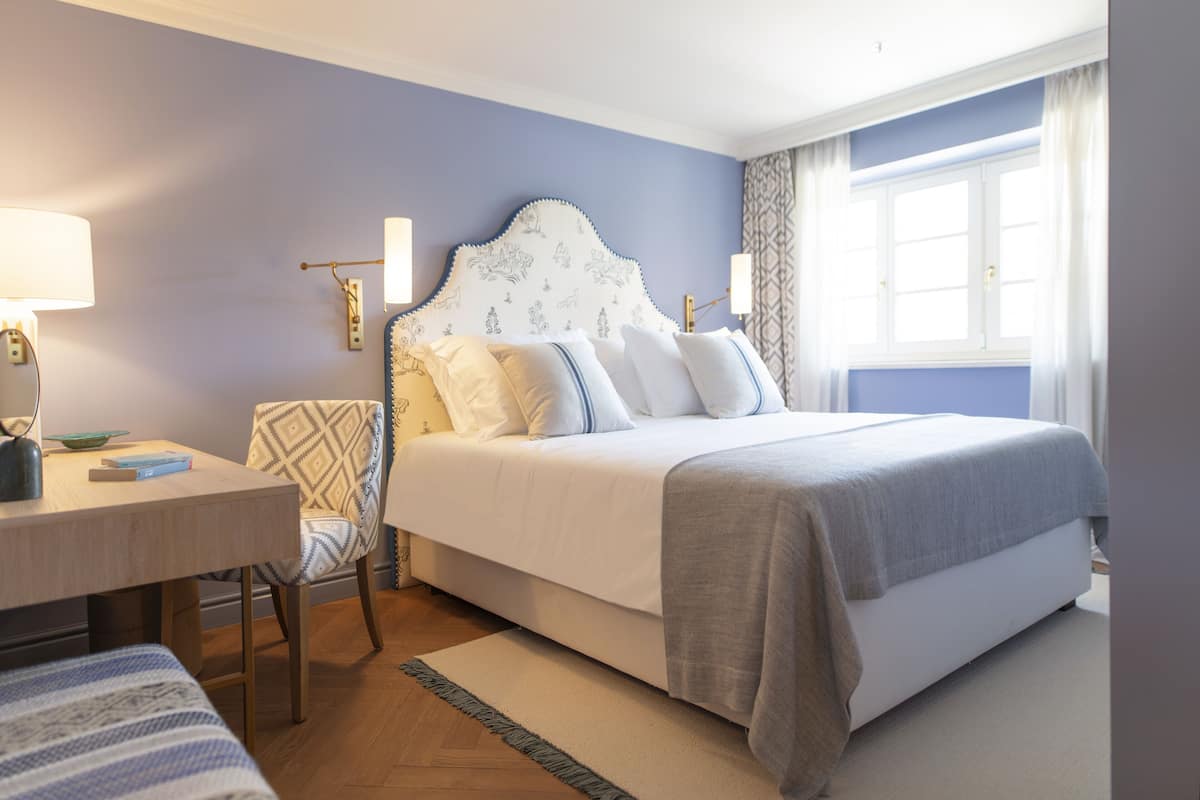 A bedroom with a bed, bedside table, chair, and a window with curtains.