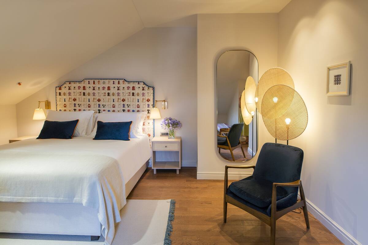 A bedroom with a bed, bedside table, lamp, chair, and a mirror.