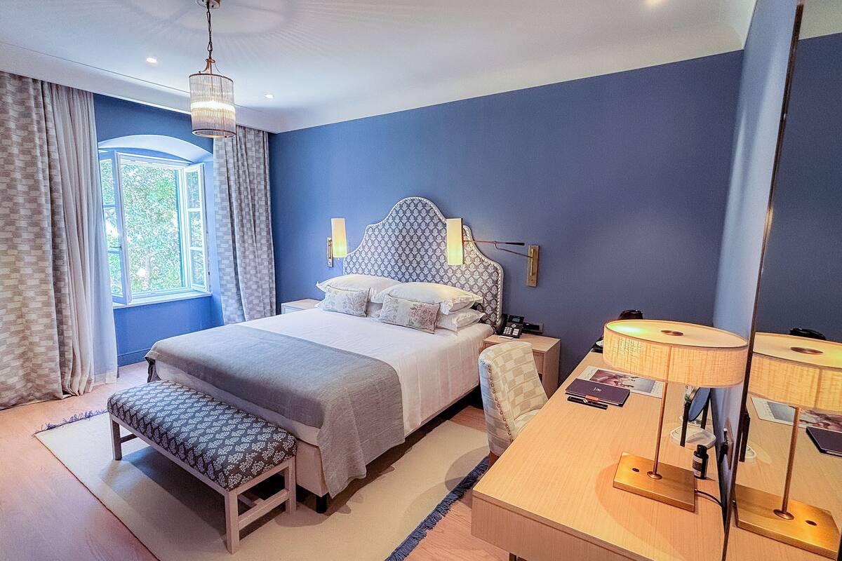 A bedroom with a bed, bedside table, lamp, and a bench.