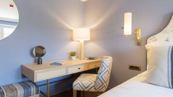 Habitación de hotel con cama, escritorio con lámpara, una silla, espejo y lámpara de pared.