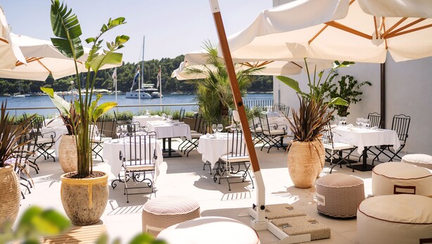 An outdoor dining area with tables and chairs, large potted plants, and umbrellas. - Hotel Supetar Cavtat (Konavle)