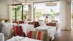 A restaurant with tables set for dining, large windows, and outdoor umbrellas. - Hotel Supetar Cavtat (Konavle)