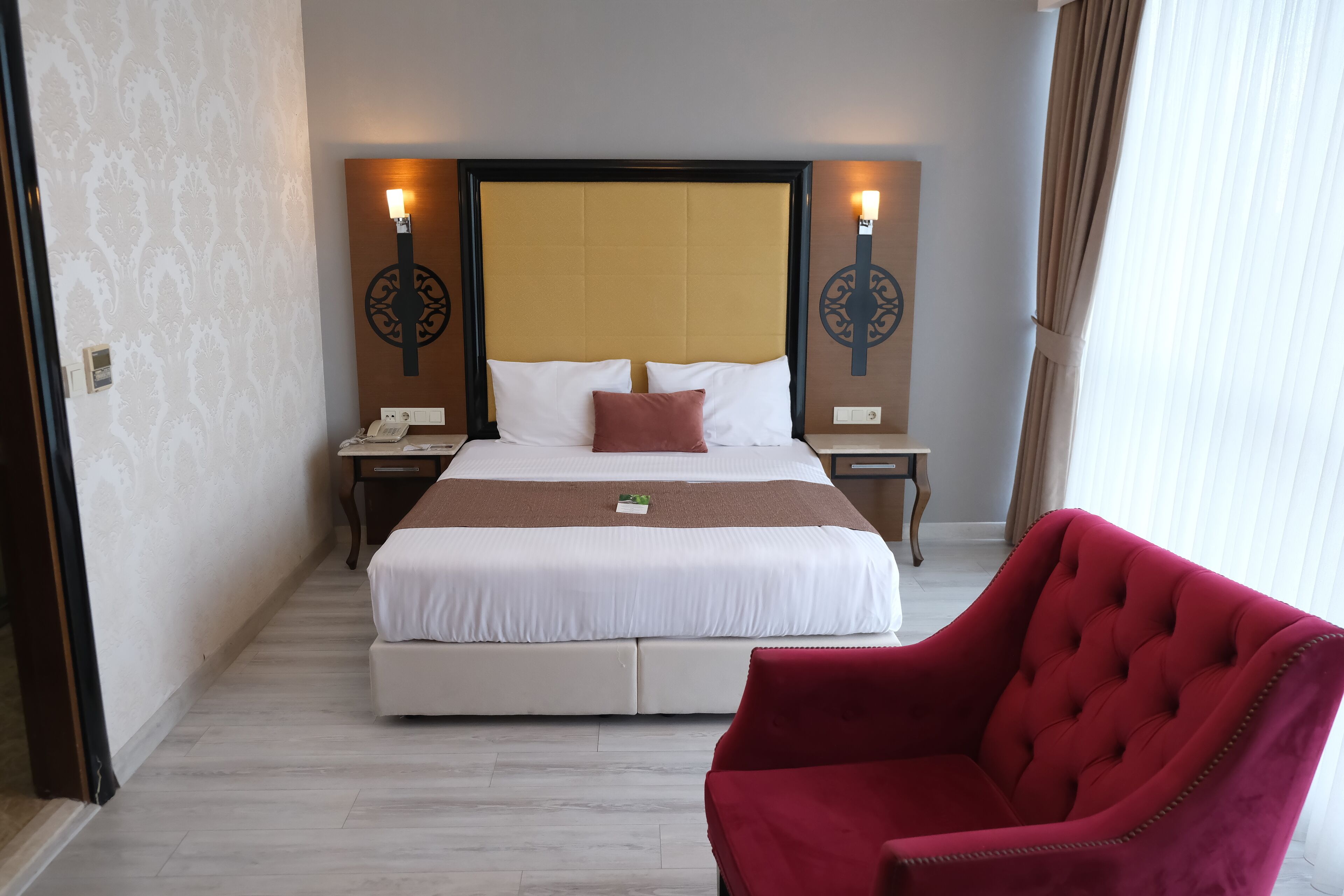 A hotel room with a large bed, two bedside tables, a red armchair, and decorative wall sconces.