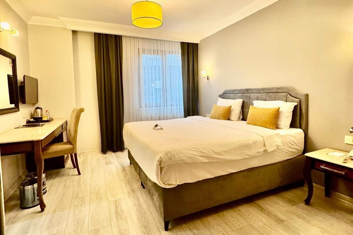 A hotel room with a bed, a desk, a chair, a small table, and a window with curtains.