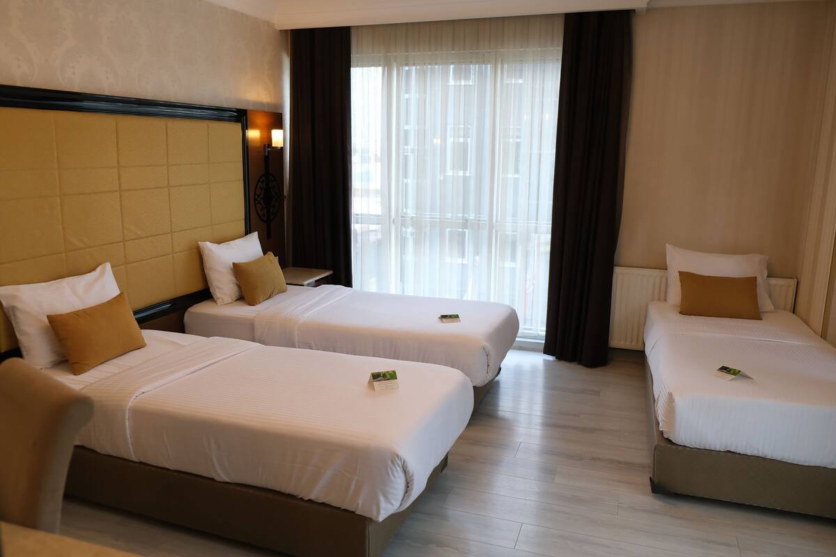 A hotel room with two single beds, a large window with sheer curtains, and a wooden floor.