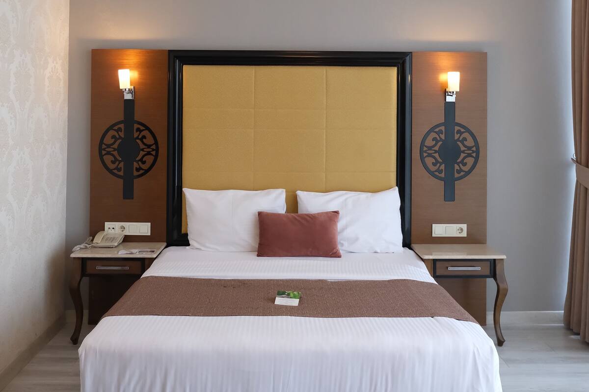 A hotel room with a large bed, two bedside tables, a wall-mounted lamp, and a telephone on the left side.