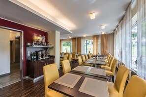A hotel dining area with long tables, yellow chairs, and a bar with various bottles. - Hotel Lousberg (Aachen)