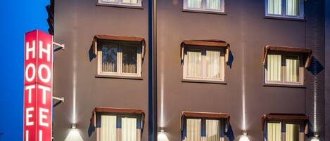 Un edificio de hotel con múltiples ventanas, un llamativo letrero que dice 'HOTEL' y una entrada bien iluminada.