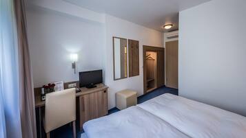 A hotel room with a bed, a desk with a computer, a chair, a TV, a mirror, and a wardrobe.