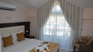 Una habitación de hotel con cama, ventana con cortinas, un sillón floral y un equipo de aire acondicionado.