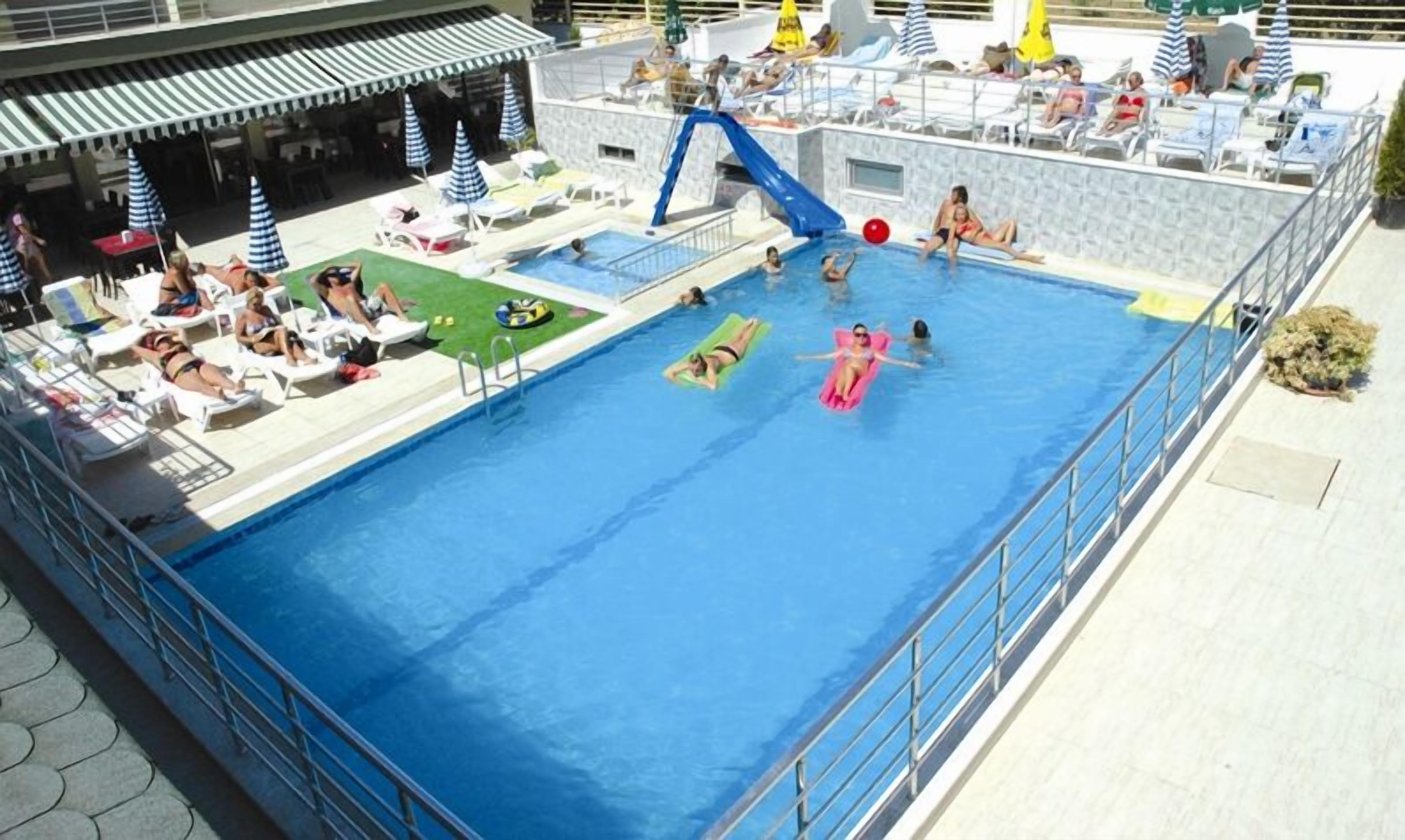 Zona de piscina con sillas de descanso, sombrillas y un tobogán.