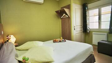 A neatly made bed with a tray of breakfast items, a hanging coat, and a bedside lamp in a room with green walls and a window.