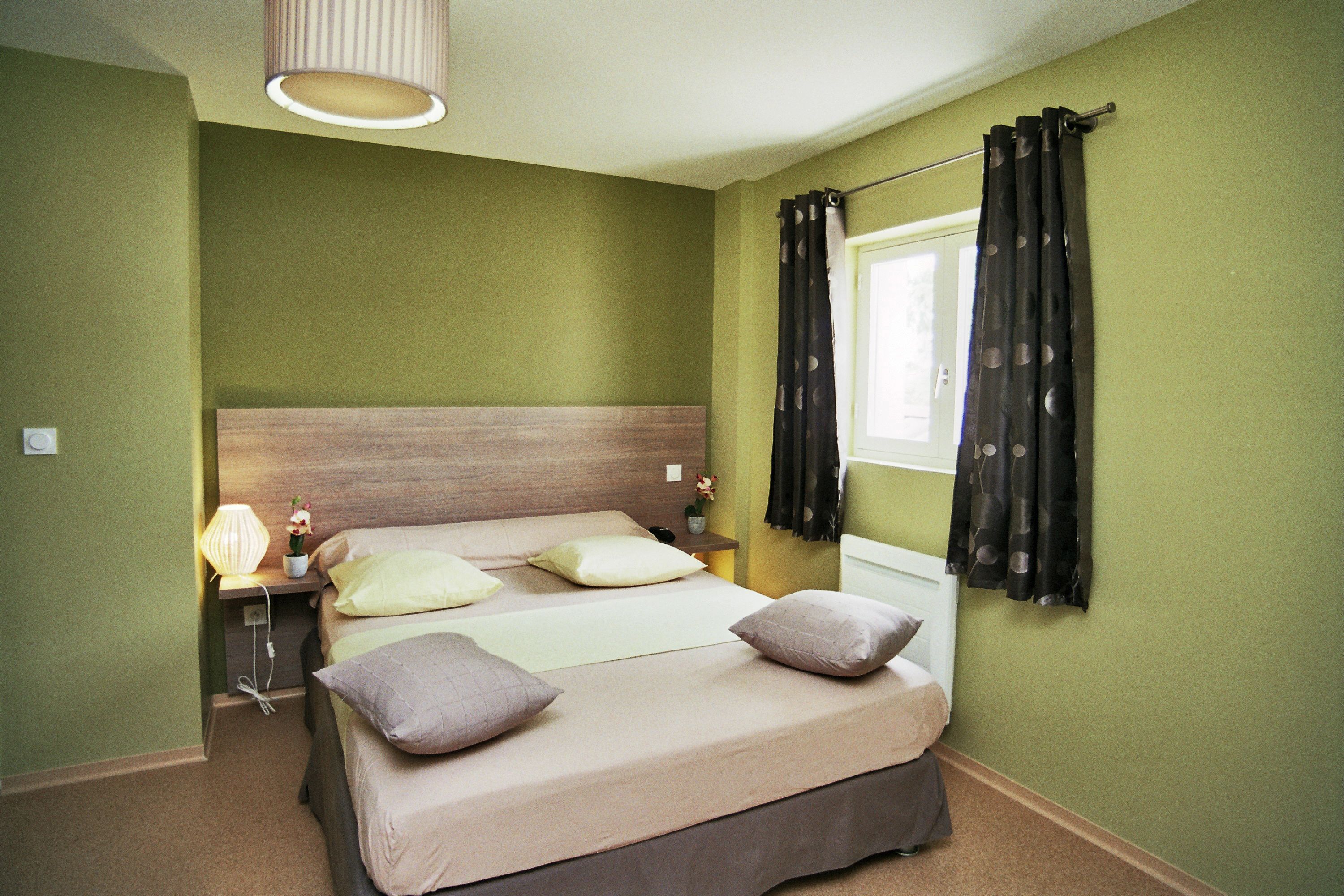 Un dormitorio con cama, mesitas de noche, lámpara y ventana con cortinas.