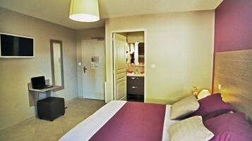 Habitación de hotel con cama, escritorio con computadora portátil, espejo y puerta que da a un baño.