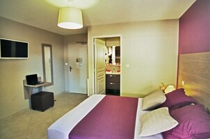 Habitación de hotel con cama, escritorio con computadora portátil, espejo y puerta que da a un baño.