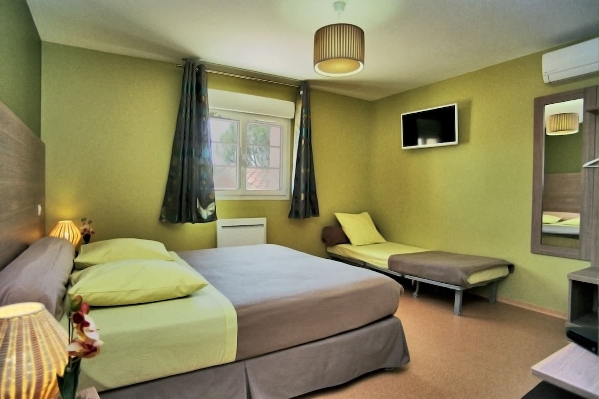 A bedroom with a large bed, a smaller bed, a bedside table, a lamp, and a window with curtains.