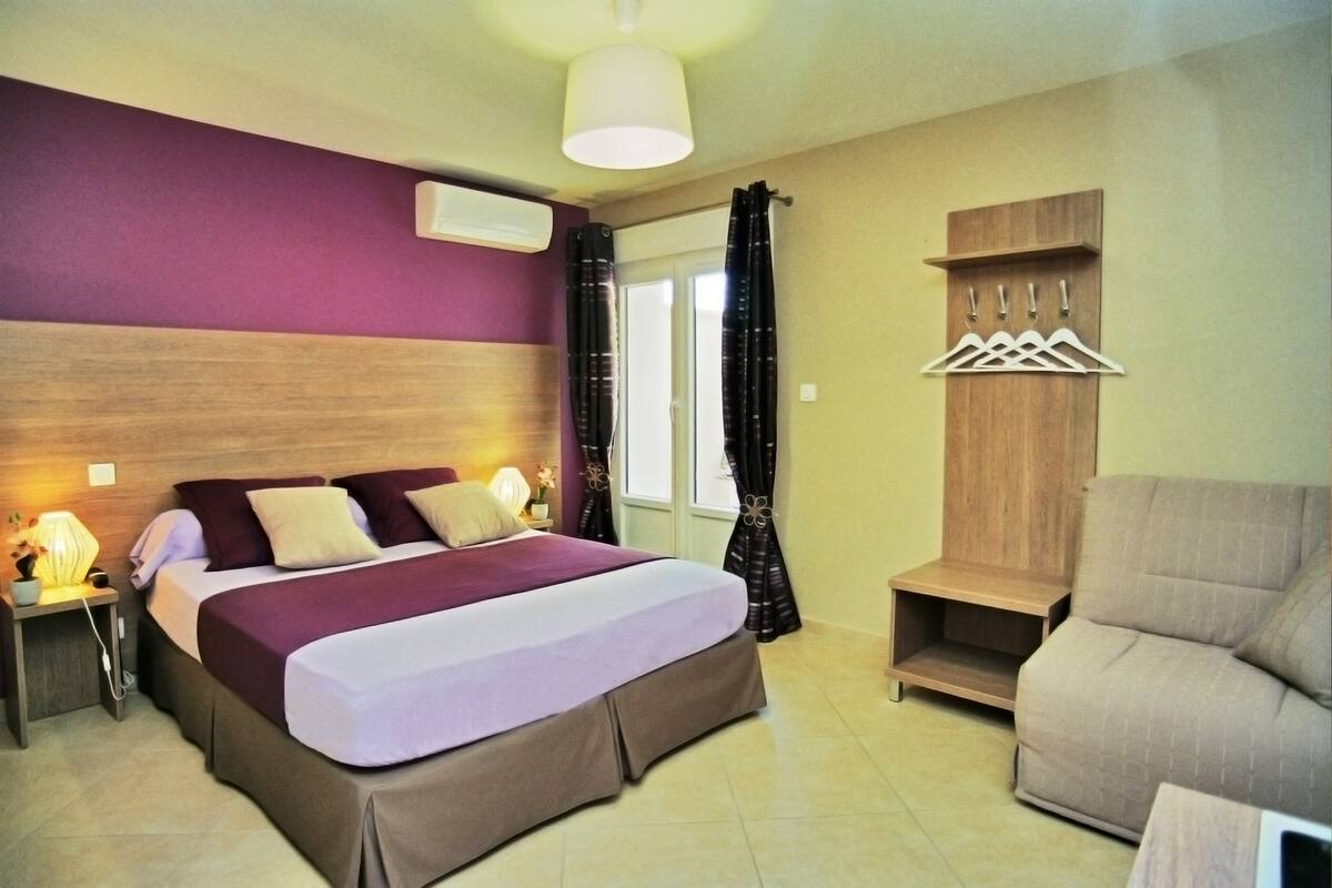 A hotel room with a bed, a nightstand, a chair, a wardrobe, and a coat rack.