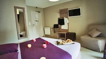 Quarto de hotel com duas camas, área de estar com sofá, televisão e uma pequena mesa com itens de café da manhã.