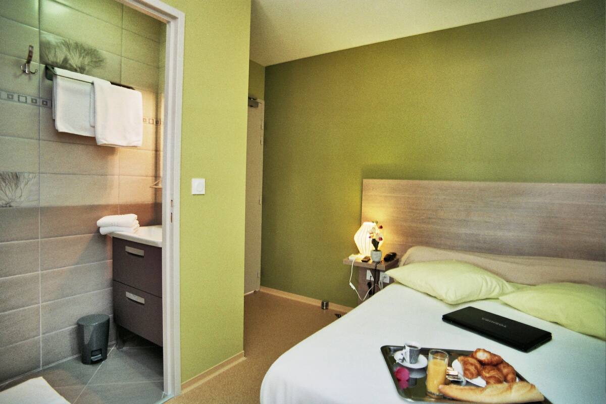 A hotel room with a bed, bedside table, lamp, and a tray with food.