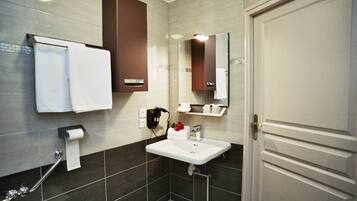 A modern bathroom with a white sink, dark tiled walls, a towel rack, a mirror, and a door.