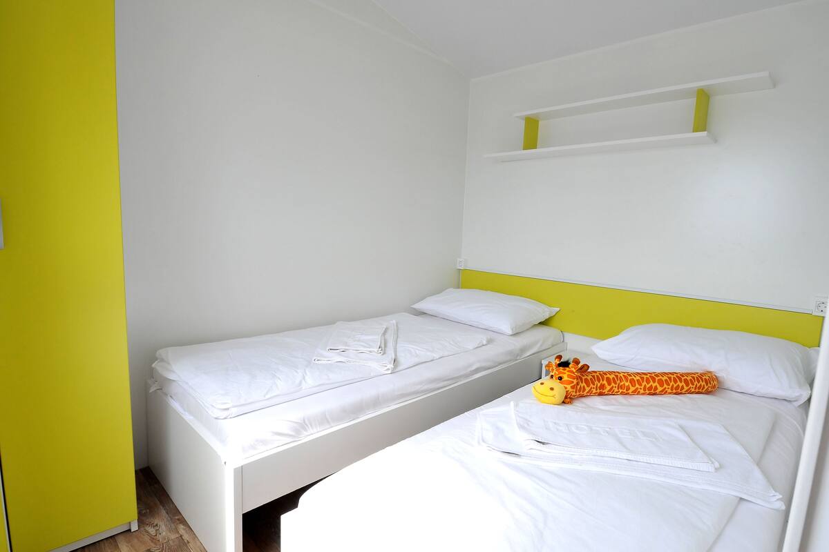 Un lit simple avec une literie blanche et un jouet en forme de girafe posé dessus.