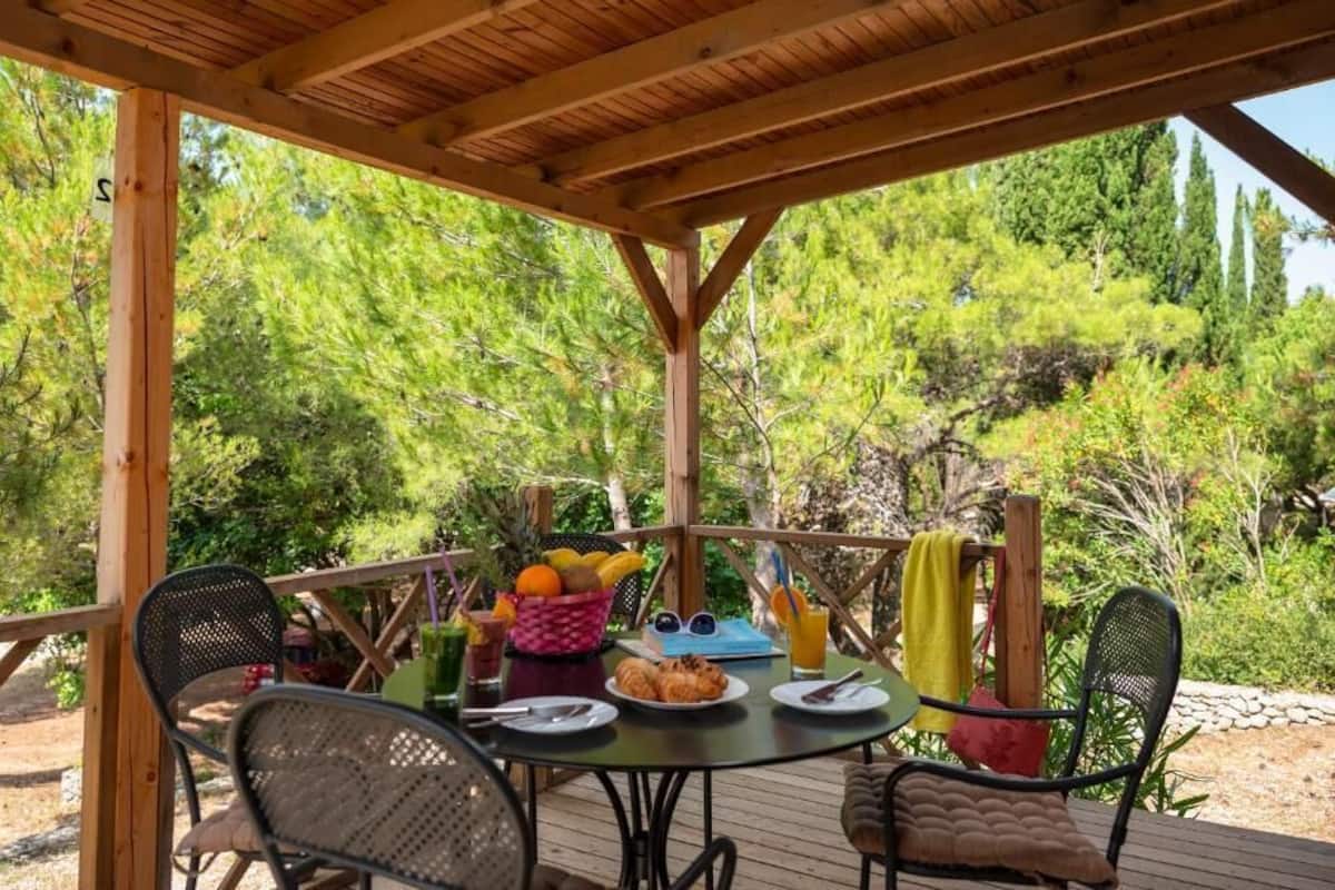 A wooden deck with a table set for breakfast, surrounded by chairs, overlooking a forested area.