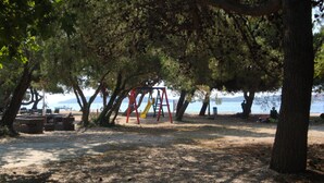 Un parque con un área de juegos, bancos y vistas al mar.