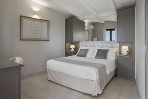 Quarto arrumado com uma cama, mesas de cabeceira, uma escrivaninha e uma obra de arte emoldurada na parede.
