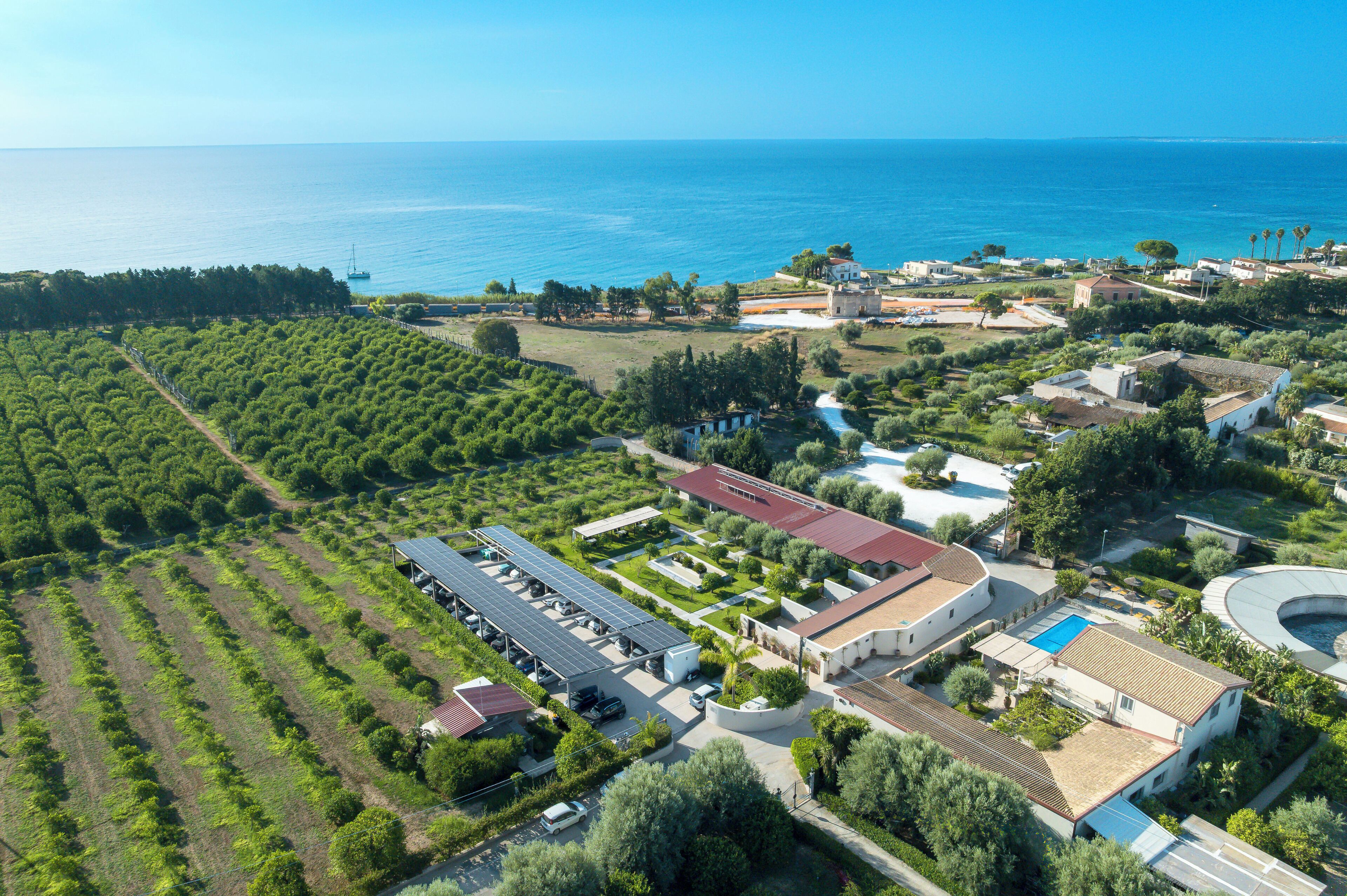 An aerial view of a coastal property with a large building, solar panels, and a swimming pool.
