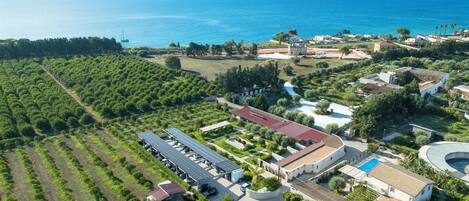 An aerial view of a coastal property with a large building, solar panels, and a swimming pool.